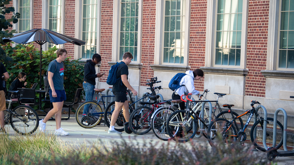 Four college male students locking up and putting their bikes on a bike rack